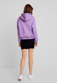 Fialová mikina s kapucí a šňůrkou, spárovaná s černou mini sukní. Bílé tenisky doplňují celý outfit.