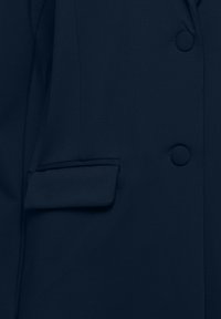 Tumsīgi zils pielāgots žakets ar vienu kabatu ar atloku un apaļiem pogām. Audums ir gluds ar neredzamām rakstām.