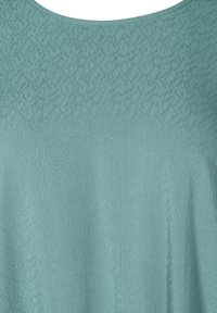 Haut bleu sarcelle clair en tissu texturé avec un motif subtil. Présente un col rond et une coupe ample et fluide.