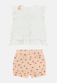 Hvid top med flæser på ærmerne og knaplukning bagpå, parret med lyserøde shorts med kirsebærtryk og elastisk talje.