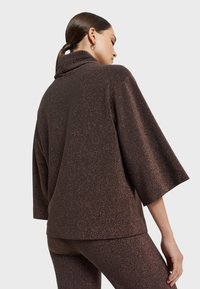 Braunes, glitzerndes Langarmoberteil mit hohem Kragen und weiten Ärmeln. Verfügt über einen strukturierten Stoff mit Funkeln, kombiniert mit passenden glitzernden Hosen.