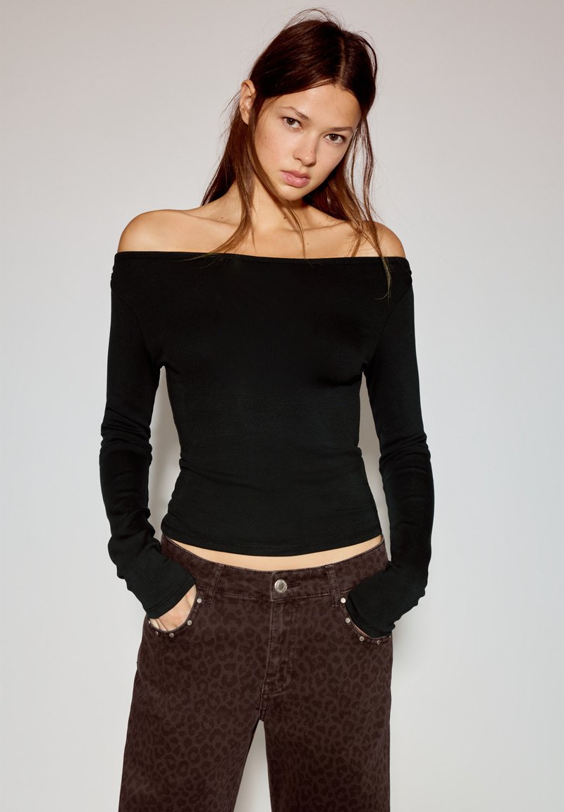 Czarny, długi rękaw, top odsłaniający ramiona, w połączeniu z brązowymi dżinsami w panterkę. Top ma dopasowany krój i prążkowaną fakturę.