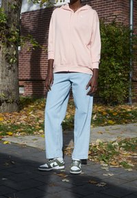 Světl růžová mikina na zip, volné světle modré džíny a zeleno-bílé tenisky. Materiál vypadá hladce a střih je pohodlný.