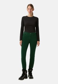 Zelené manšestrové kalhoty s úzkým střihem, vysokým pasem a designem s pěti kapsami, doplněné černým dlouhým rukávem a černými šněrovacími botami.