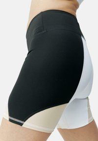 Shorts de sport colorés en noir, blanc et beige, à taille haute, fabriqués dans un matériau extensible et dotés de coutures contrastées.
