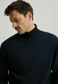 Ciemnogranatowy sweter z golfem wykonany z miękkiego materiału, z subtelnym logo na piersi i teksturowanym prążkowanym dekoltem.