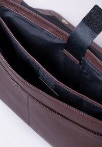 Brown leather tote bag with a black interior, featuring two compartments and a Velcro strap, highlighted by fine stitching details.