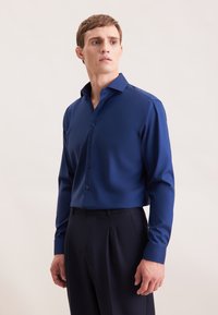 Blauwe lange mouwen overhemd met een spreidkraag, gemaakt van soepel stof. Bevat donkere knopen en aangesloten mouwen, gecombineerd met donkere broeken.