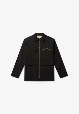 Melns džemperis no kokvilnas ar rāvējslēdzēju priekšā, diviem priekšējiem kabatām un ar tekstu "PAS DE MONACO" izšūtu zeltainā krāsā uz kreisā krūšu.