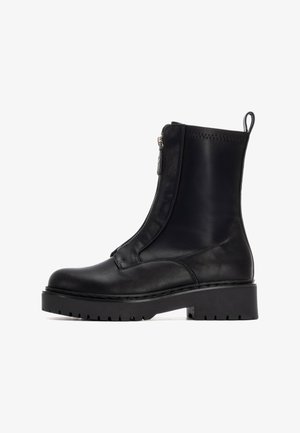 Bottes noires en cuir à chevilles avec une semelle épaisse et robuste, fermeture à glissière et une languette à l'arrière. Texture lisse et design minimaliste.