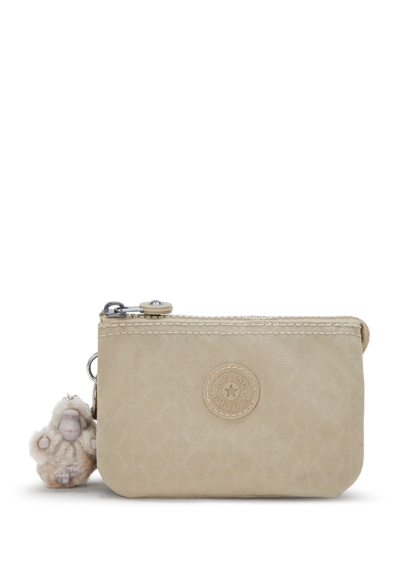Funda de nylon beige con un acabado texturizado, que cuenta con un cierre de cremallera, un acento con el logo y un llavero decorativo de un mono de peluche adjunto.