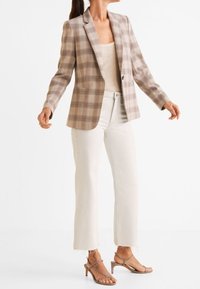 Blazer à carreaux dans des tons beiges avec une coupe structurée, associé à un jean blanc court et des talons brun avec des brides. Le tissu est lisse et léger.