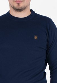 Maglione blu navy con col rotondo, realizzato in un tessuto testurizzato. Presenta un piccolo logo marrone sul lato sinistro del petto.