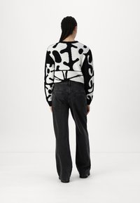 Zwarte en witte geblokte sweater met een oversized ontwerp, gecombineerd met zwarte high-waisted jeans met achterkantzakken en een relaxed fit.