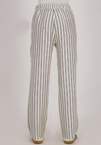Witte broek met verticale marineblauwe strepen, voorzien van een elastische tailleband en een losse pasvorm. Het materiaal heeft een gestructureerd oppervlak.