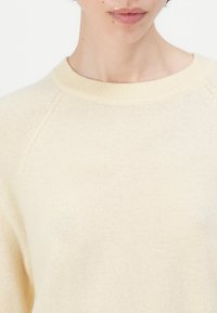 Kreemivärvi kootud särk ümmarguse sooniku kaelusega, pehme tekstuuriga ja raglaanvarrukatega. Kangas näeb välja sõmer ja minimalismi nüanssidega.
