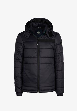 Chaqueta acolchada negra con capucha, que cuenta con un cierre frontal, bolsillos laterales y puños acanalados, combinada con jeans de mezclilla azules y zapatillas blancas.