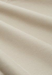 Tissu beige texturé avec un motif en chevrons subtil, affichant des fibres tissées lisses et une apparence uniforme sur toute la surface.