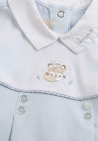 Vêtement bleu clair avec un col blanc, un design de renard brodé, des coutures décoratives et deux boutons en bas.