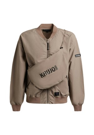 Beżowa bomberka zapinana na zamek błyskawiczny z prążkowanymi mankietami i kołnierzem, wyposażona w dopasowaną torbę na ramię z czarnym nadrukiem "KHUJO 2001".