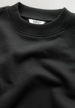 Black sweatshirt with ribbed crew neck, smooth texture, and a folded design. Label reads "NEXT," visible in white on the inner collar.