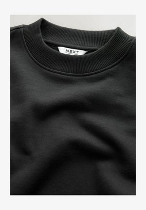 Svart sweatshirt med ribbat rundhals, slät textur och vikt design. Etiketten läser "NEXT", synlig i vitt på den inre kragen.