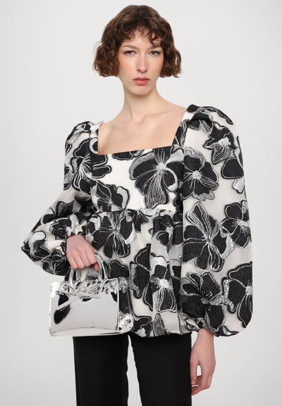 Blusa de peplum floral en blanco y negro con mangas abullonadas, combinada con un pequeño bolso plateado de diseño estructurado.
