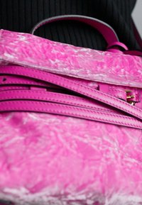 Borsa a tracolla rosa con finitura liscia, caratterizzata da un design strutturato, dettagli delle fibbie piegati e una maniglia superiore per il trasporto.