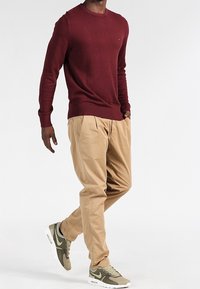 Kastanjebrun tröja med ribbade muddar och halsringning, tan färgade veckade byxor och olivgröna sneakers. Outfiten kombinerar neutrala och jordnära toner.