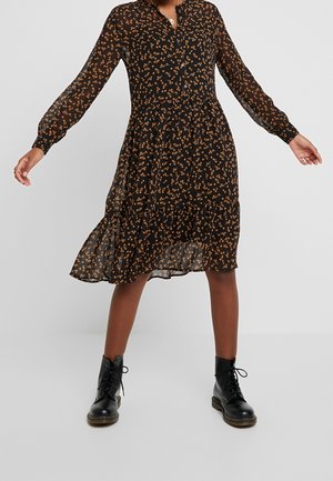 Robe noire à motifs floraux avec de longues manches transparentes, une patte de boutonnage et une jupe à volants ; ornée d'un imprimé floral orange et portée avec des bottines noires.