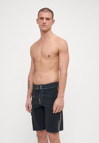 Shorts de bain noirs avec des accents orange, taille élastique avec cordon de serrage et couture contrastée. Fabriqués dans un matériau léger, design à longueur de genou.