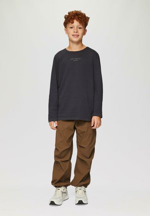 Ciemnoszara koszula z długim rękawem z napisem "EASY MINDSET", w połączeniu z beżowymi spodniami typu cargo i jasnymi sneakerami, stojąca na jednolitym tle.