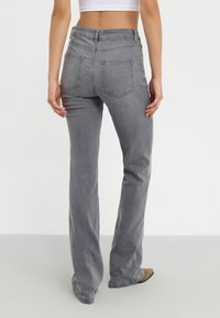 Harmaat farkut suoran leikkauksen omaavina. Ominaisuuksiin kuuluvat kaksi takataskua ja keskikorkea vyötärö. Sileä rakenne ja minimaalinen yksityiskohtaisuus.