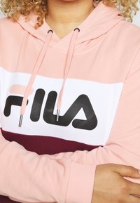Gecombineerde hoodie met een kleurenschema in roze, wit en bordeauxrood, versierd met een groot zwart "FILA"-logo en trekkoordaccenten.