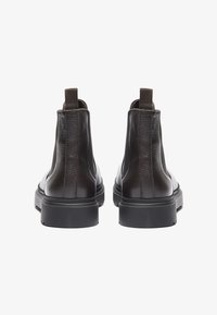 Bottines en cuir marron avec une finition texturée, des panneaux latéraux élastiques et des languettes à l'arrière. Semelles épaisses en caoutchouc noir.
