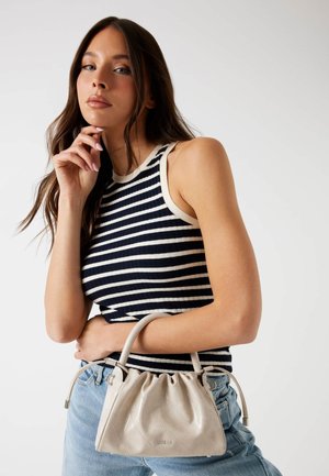 Un sac à main matelassé beige avec un design froncé et des poignées doubles, associé à un haut sans manches rayé bleu marine et blanc et un jean en denim.