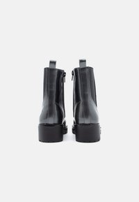 Musta nahast pahkluu saapad läikiva viimistlusega, külgmise tõmblukuga, tõmblukkude ja paksu kontsaga. Lihtne ja stiilne disain.