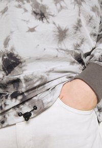 Pulóver de tie-dye en gris y blanco con un ajuste relajado, que presenta puños elásticos y un detalle de cordón en el dobladillo. Textura suave.
