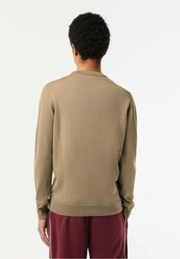 Długa sweter w oliwkowej zieleni z prążkowanym dekoltem i mankietami, o gładkiej fakturze i luźnym kroju, zestawiony z bordowymi spodniami.