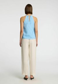 Top bluastro a halter con motivo a righe diagonali e dettaglio sul retro a forma di chiave. Abbinato a pantaloni larghi di colore crema e scarpe slip-on nere.