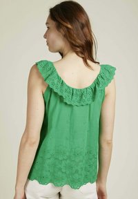 Haut sans manches vert avec un col en dentelle festonnée et à œillets, et une broderie florale le long de l'ourlet, fabriqué en tissu léger.