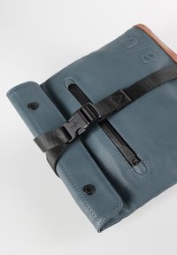 Blaue Ledertasche mit braunem Lederakzent, ausgestattet mit einem schwarzen Schnallenriemen und einem Reißverschluss. Einfaches, rechteckiges Design mit verstärkten Nähten.