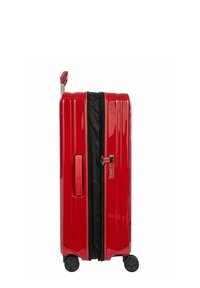 Valigia rigida rossa con finitura lucida, scanalature verticali, zip nera, lucchetto a combinazione, manico telescopico e quattro ruote girevoli.