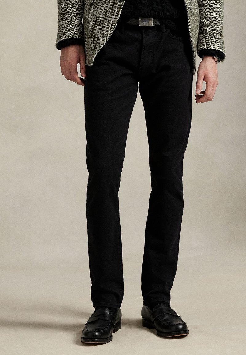 Svarte denimbukser, tettsittende stil, midt på livet, klassisk fem-lomme design, kombinert med svarte loafers. Teksturert overflate, subtil glans.