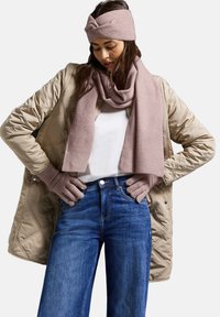 Beige kviltad kappa, ljusrosa ribbad scarf och huvudband, mörkblå jeans och rosa handskar, som visar en avslappnad lager-på-lager-outfit.
