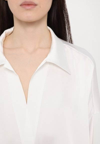 White satin blouse with a pointed collar, featuring a v-neckline and soft, smooth texture. Notable for its clean lines and minimal design.