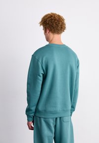 Teal sweatshirt met een ronde hals en ribgebreide manchetten. De stof heeft een gladde textuur en toont een casual ontwerp met een comfortabele pasvorm.