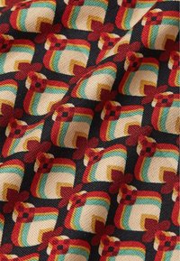 Tessuto con un motivo geometrico colorato nei toni crema, rosso, verde e nero; texture intrecciata con quadrati in rilievo e accenti floreali.