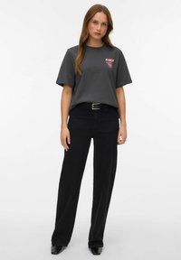 Szara bawełniana koszulka z krótkim rękawem i różowym nadrukiem na piersi, zestawiona z czarnymi, szerokimi spodniami z wysokim stanem.