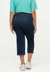 Tummansiniset lyhyet farkut korkealla vyötäröllä, joissa on perinteinen viiden taskun muotoilu ja siistit helmat, yhdistettynä turkoosiin T-paitaan ja valkoisiin tennareihin.